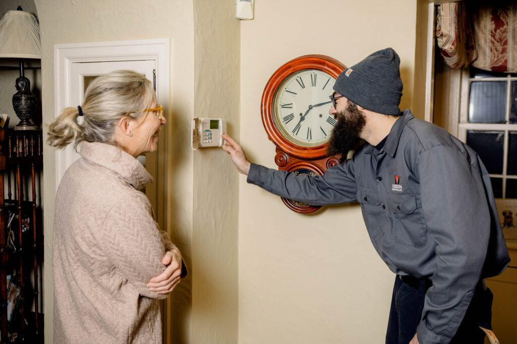 Vision Mechanical employee showing customer thermostat in residential home